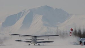 Lite propellfly på snødekt rullebane med fjell i bakgrunnen