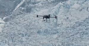 En drone flyr foran en bratt, isdekket fjellvegg